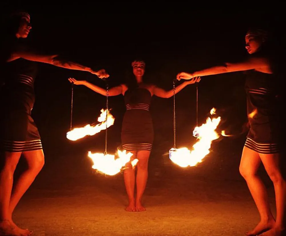 Three performers are swinging fiery poi in a coordinated fire dance performance at night