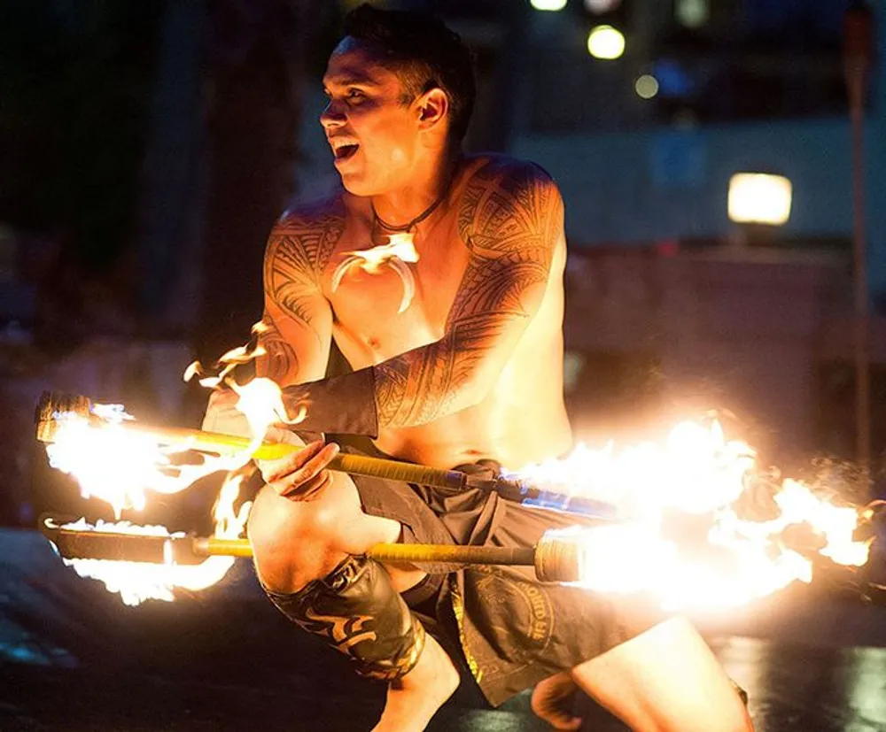 A performer with traditional tattoos is demonstrating a fire dance at night skillfully manipulating flaming objects