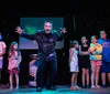 A performer enthusiastically entertains a group of children on stage under a starry light backdrop