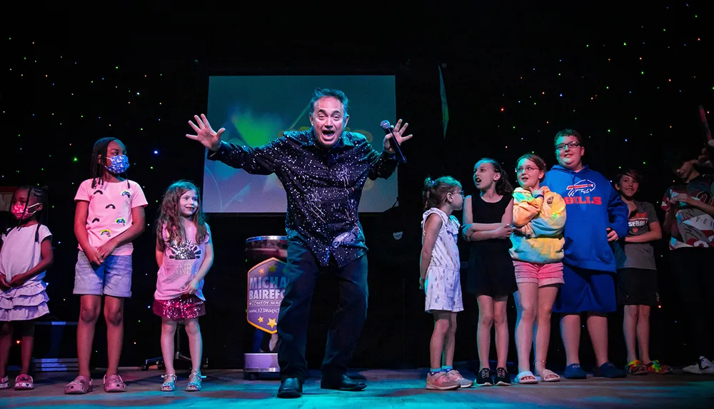 A performer enthusiastically entertains a group of children on stage under a starry light backdrop