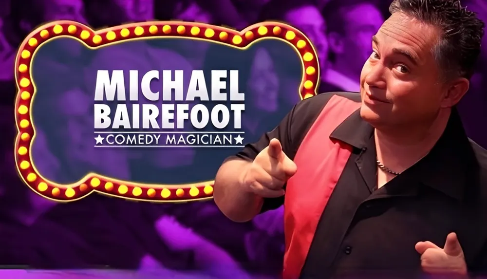 A man poses in front of a sign that reads Michael Bairefoot Comedy Magician with a background of enthusiastic audience members
