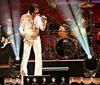 The image depicts a person dressed as a tribute artist performing onstage imitating a famous musician alongside text that says Elvis Tribute Show