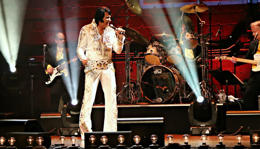 A person dressed as an Elvis Presley impersonator performs on stage with a band under colorful stage lighting