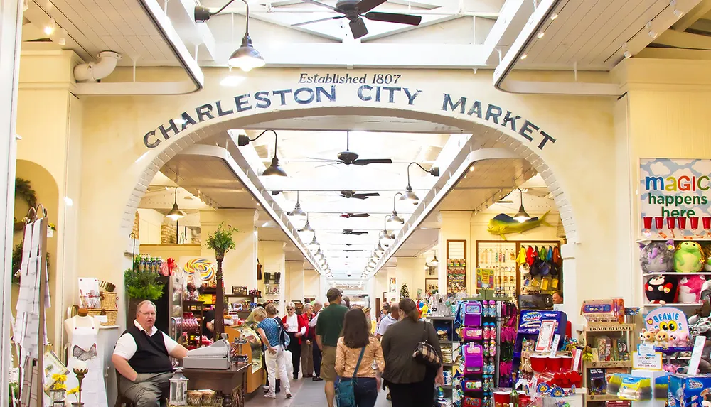 This image captures a bustling indoor market scene with an arch reading CHARLESTON CITY MARKET indicating it is a historic marketplace established in 1807 where patrons are shopping and browsing various goods