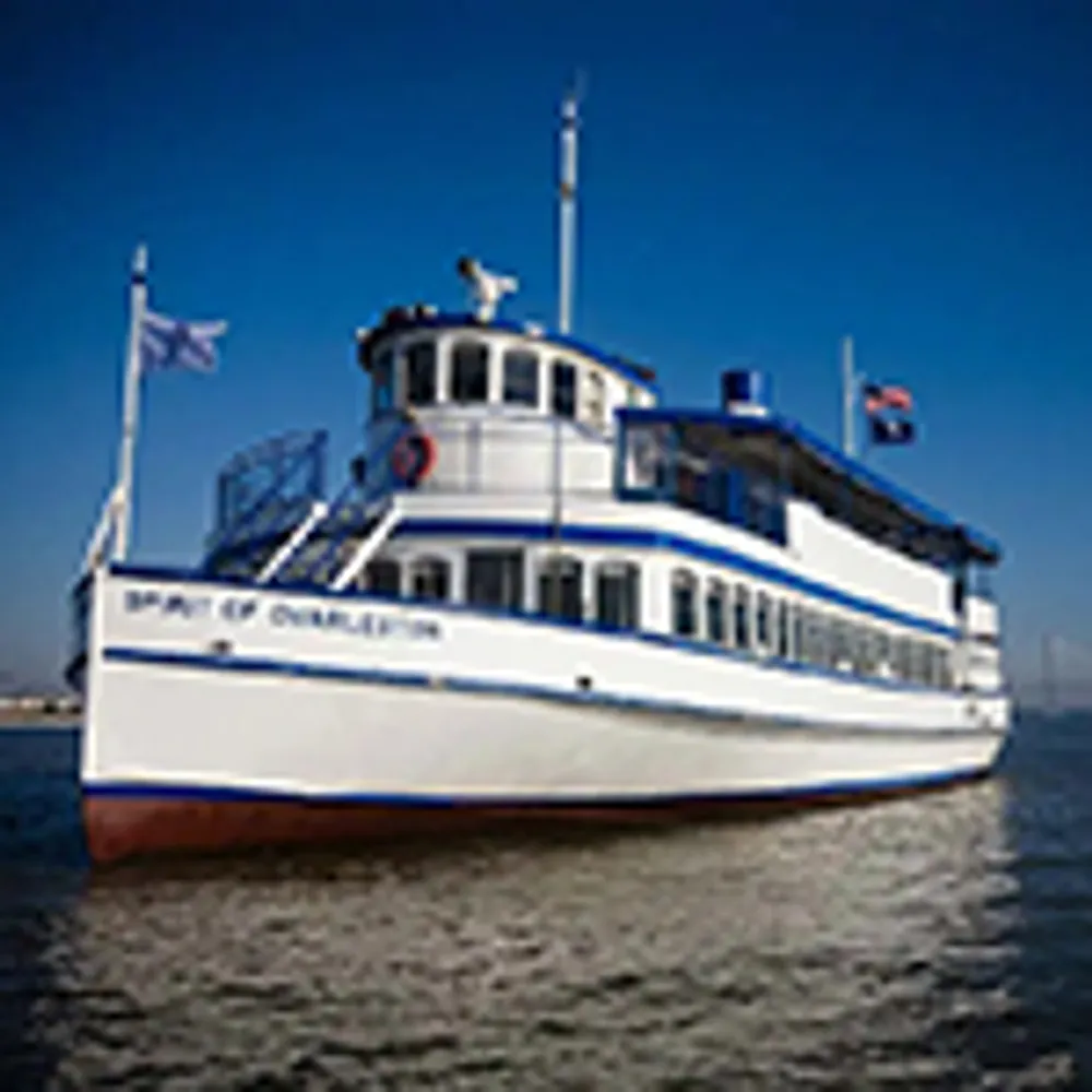 The image shows a white and blue ferry boat named Spirit of Charleston sailing on the water with flags flying from its mast