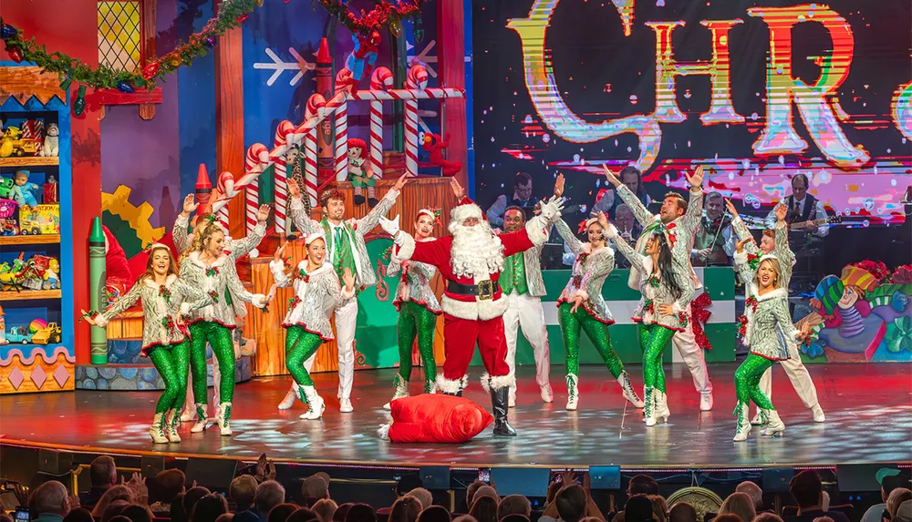 A Christmas-themed stage performance features Santa Claus and a group of festive dancers in colorful costumes