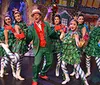 Two performers in festive costumes express excitement on a colorful holiday-themed stage