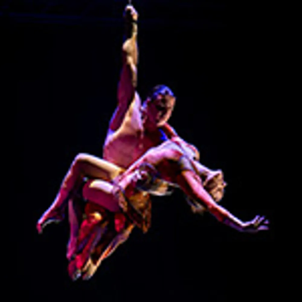 Two aerial performers are gracefully suspended in mid-air against a dark background