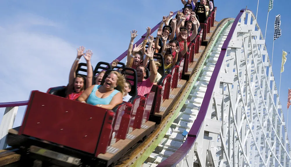Thrilled passengers raise their hands as they experience the exciting descent on a wooden roller coaster