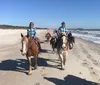 A group of people are horseback riding along a beach with a pier in the background