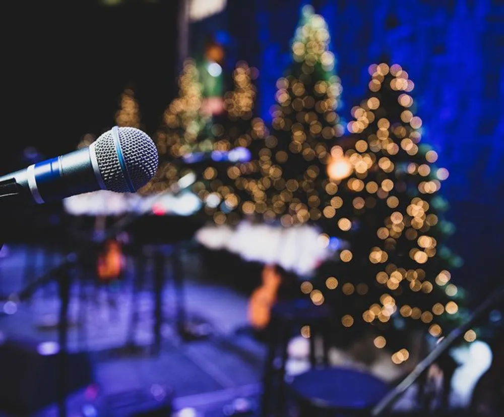 A microphone in sharp focus stands ready for a performance with a blurred backdrop of a decorated Christmas tree and musical instruments