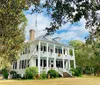 The image showcases a classic two-story white house with a double porch adorned with wreaths surrounded by a serene landscape with Spanish moss-covered trees