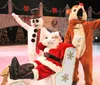 Santa Claus is lounging in a chair on an ice rink while a person in a snowman costume and another in a reindeer costume pose playfully beside him in a festive holiday setting