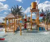 The image shows a colorful childrens water playground with various water features slides and playful structures located beside a beachfront high-rise building