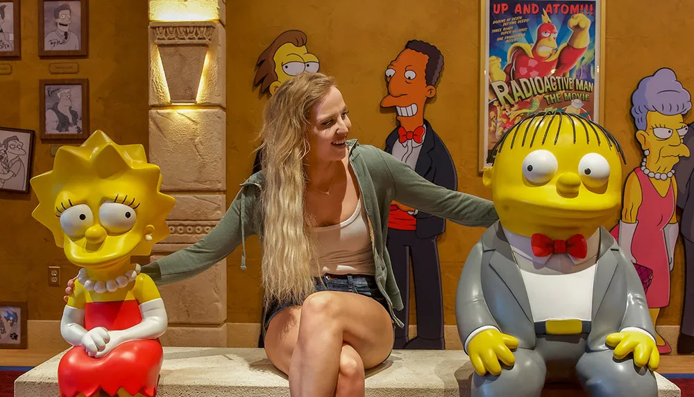 A person is sitting with life-sized models of Lisa and Milhouse from The Simpsons inside a room themed after the animated show