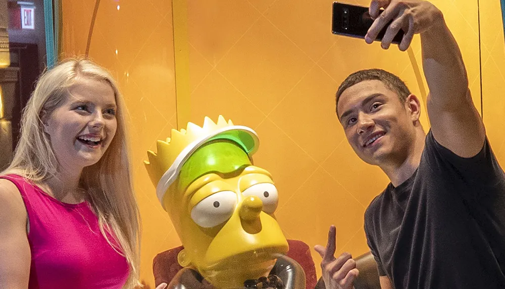 A man and a woman are taking a selfie with a life-size statue of Bart Simpson