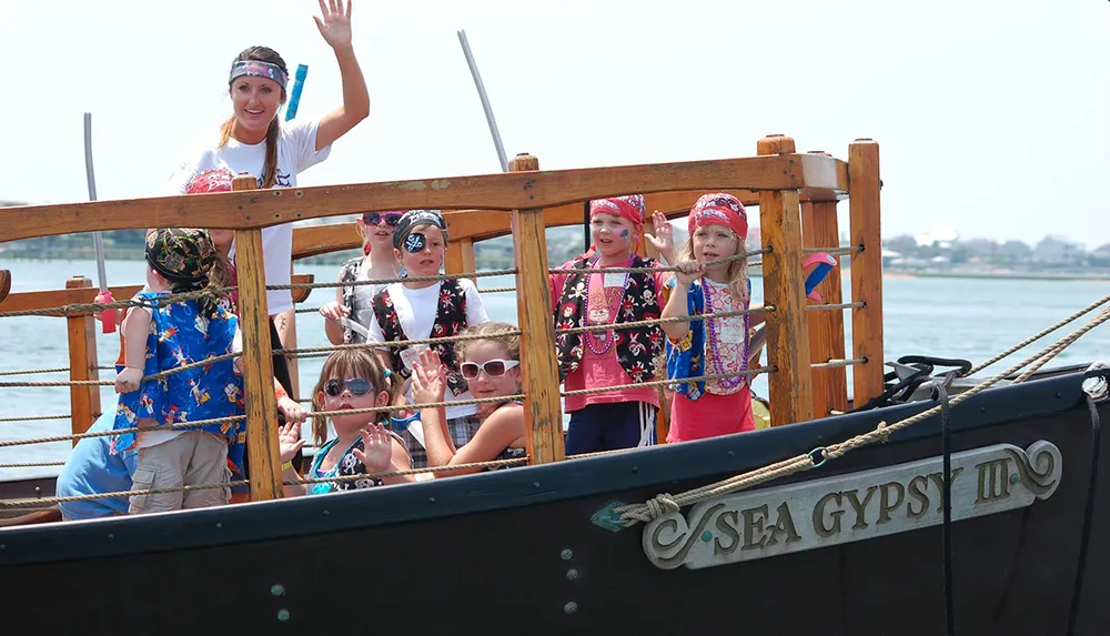 A group of children dressed as pirates are on a boat named Sea Gypsy III waving and enjoying what appears to be a themed adventure