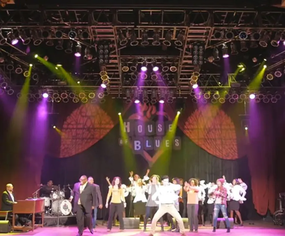 A group of people is performing on a stage with colorful lighting and a backdrop that says House of Blues