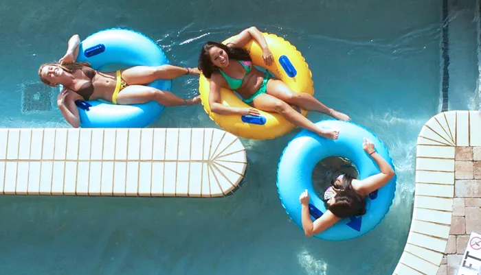 Three people are lounging on colorful inflatable rings in a swimming pool on a sunny day