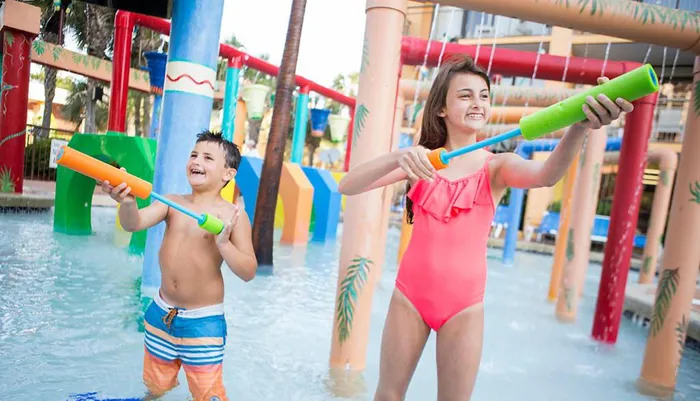 Two children are joyfully playing with water blasters at a colorful splash park