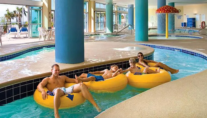 People are enjoying a lazy river ride on yellow inner tubes at an indoor pool facility