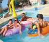 A group of people including children and adults are enjoying themselves on colorful floatation tubes in a sunny pool with a lazy river feature