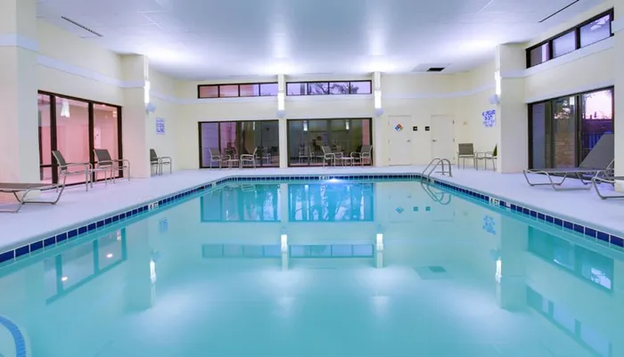 An indoor swimming pool with lounge chairs and large windows in a tranquil well-lit space