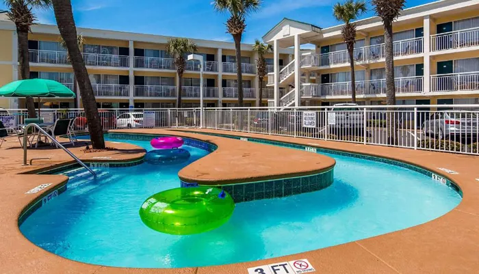 The image shows a sunny poolside scene with colorful floats surrounded by a multi-story hotel building with palm trees