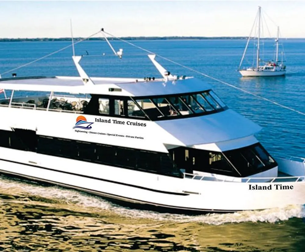 A large white cruise boat named Island Time from Island Time Cruises is sailing near the coast with another sailboat in the background under a clear sky