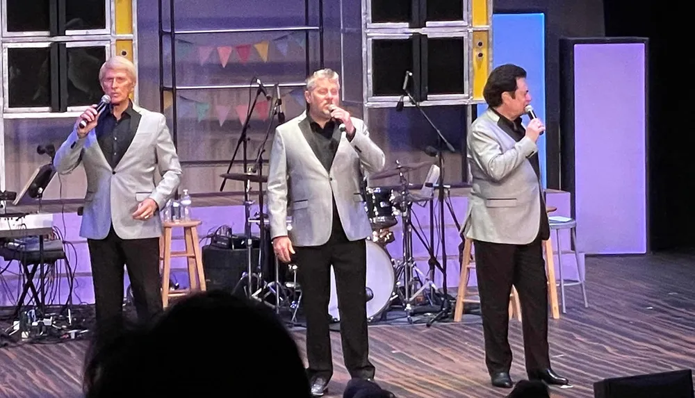 Three men in suits are performing onstage each holding a microphone and singing to an audience
