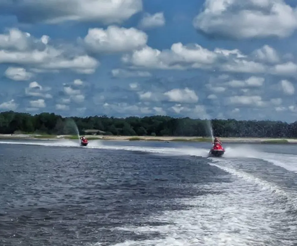 Two speedboats are racing on a river creating white wake trails behind them under a sky scattered with clouds