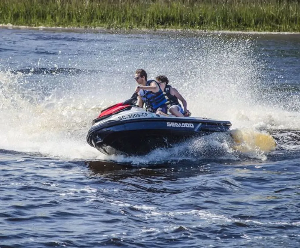 Two individuals are riding a jet ski at speed creating a spray of water behind them