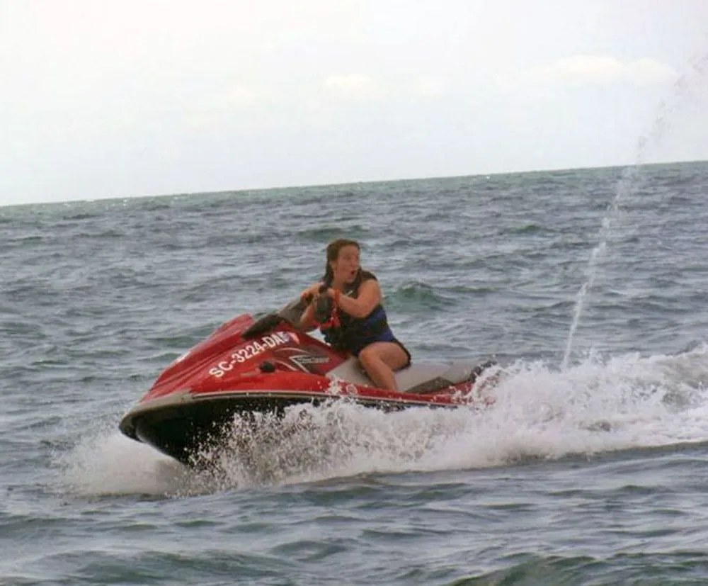 A person is riding a red jet ski with focused intensity across the choppy surface of the ocean