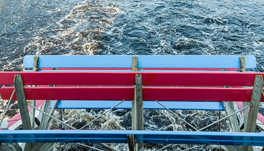 A colorful blue and red bench overlooks turbulent water suggesting a viewpoint or rest area near a body of water