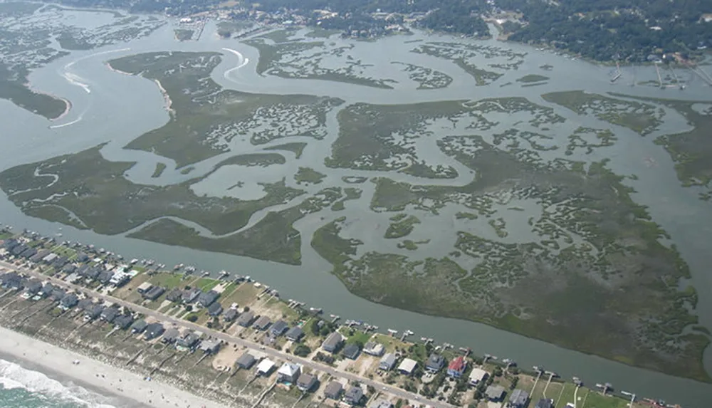 An aerial view of a coastal area showing a patterned wetland adjacent to a developed shoreline with houses