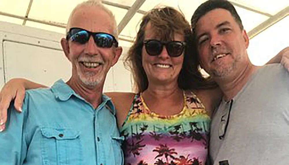 Three smiling individuals wearing sunglasses are posing closely together for a photo possibly enjoying a sunny outdoor event