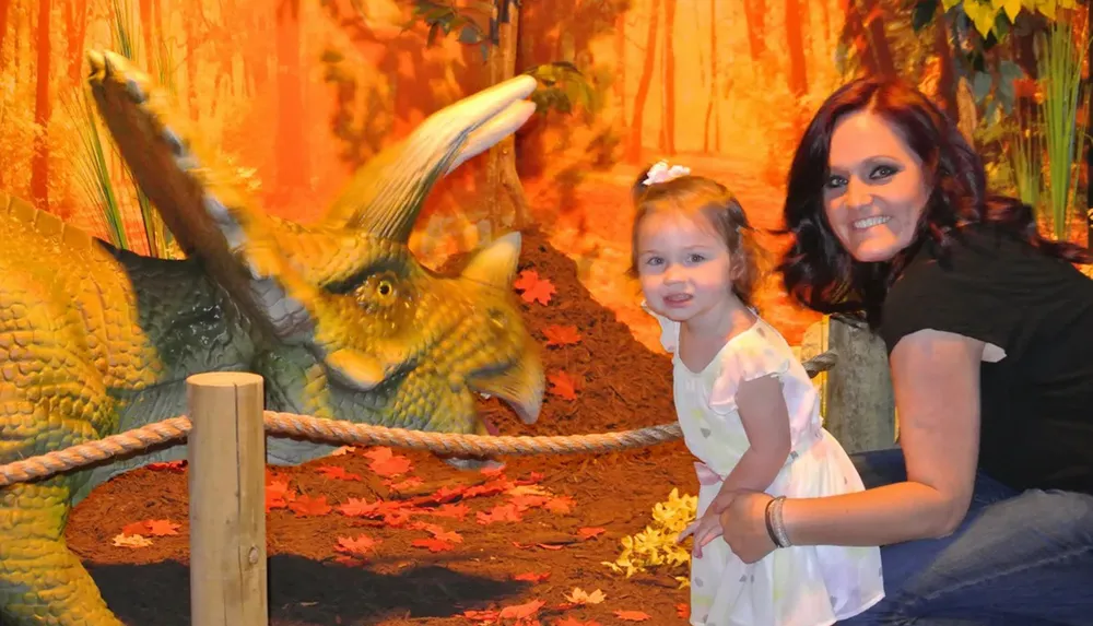 A woman and a young child are posing for a photo next to a model of a Triceratops in a themed exhibit