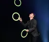 A performer is juggling glowing rings on a stage with a backdrop of bright lights