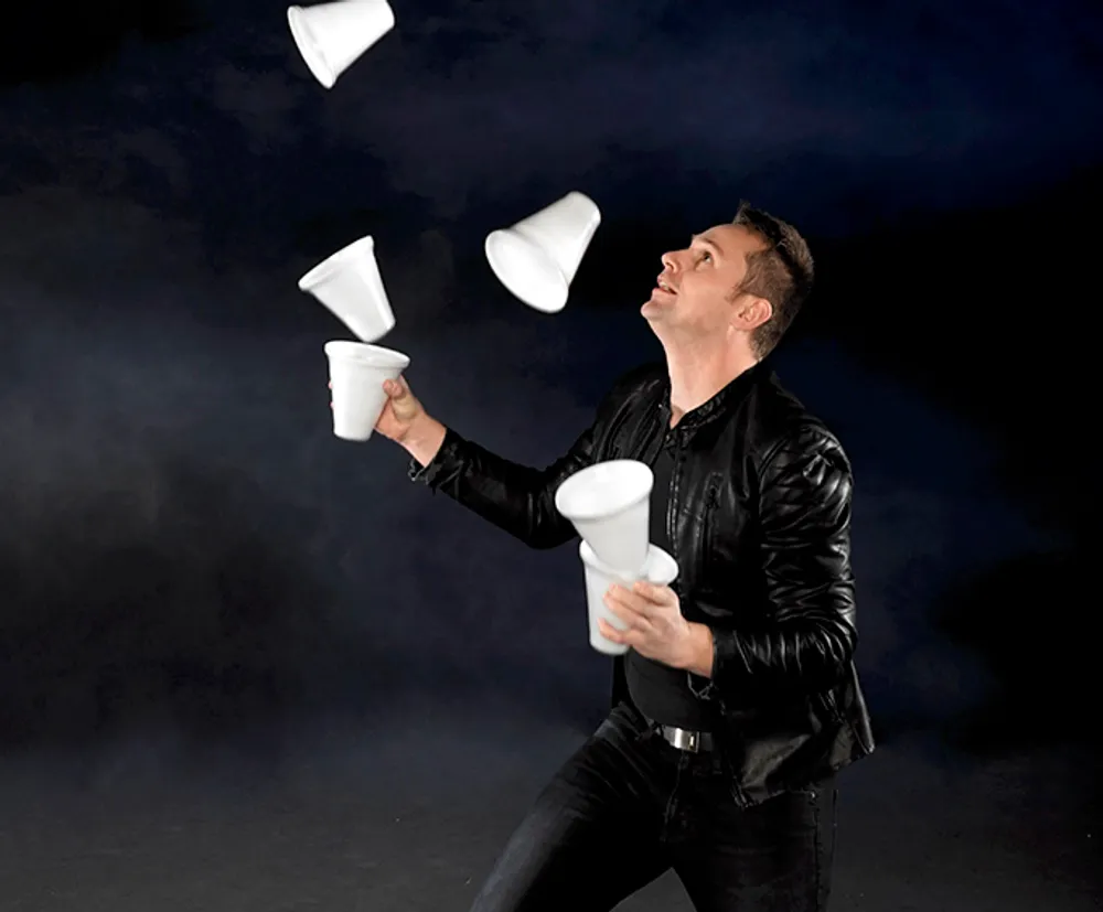A person is juggling multiple white objects that resemble megaphones or cones against a dark background