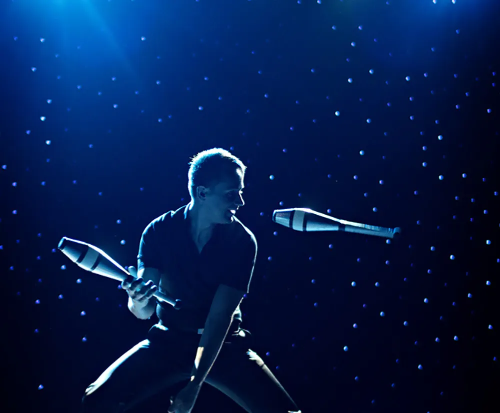 A performer is dramatically illuminated by blue stage lighting while singing into a microphone with a star-like pattern in the background