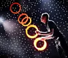 A performer is juggling glowing rings on a stage with a backdrop of bright lights