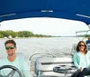 Two individuals are enjoying a ride on a blue and white pontoon boat with a blue sunshade on a calm river surrounded by trees