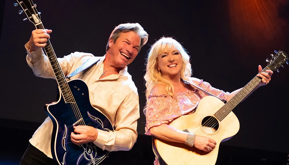 Two smiling musicians a man and a woman are performing on stage each holding a guitar