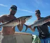 Two people are smiling on a boat proudly displaying their catch of large fish with a clear blue sky and calm sea in the background