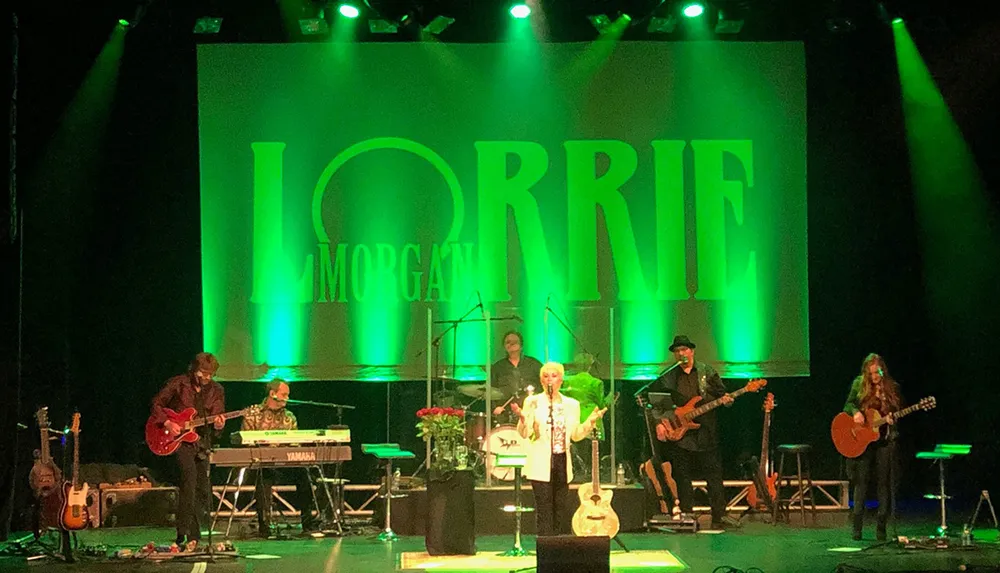 This is an image of a music concert where a band is performing on stage with a large illuminated backdrop displaying the name LORRIE MORGAN