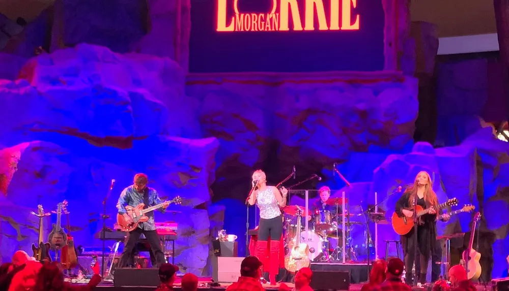 A band performs on stage with a rugged rock-like backdrop and colorful lighting