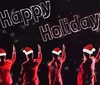 The image shows four individuals in red with Santa hats raising their hands in a performance pose against a dark background with snowflakes and the text Happy Holidays