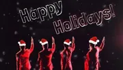 The image shows four individuals in red with Santa hats raising their hands in a performance pose against a dark background with snowflakes and the text 
