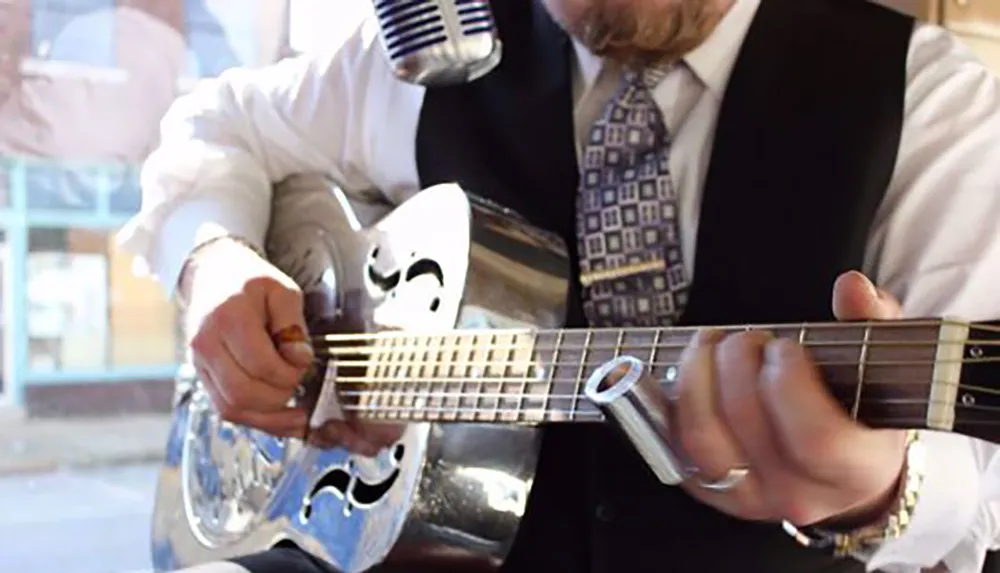 A musician in formal attire is playing a resonator guitar and a microphone is positioned close to him to capture the sound