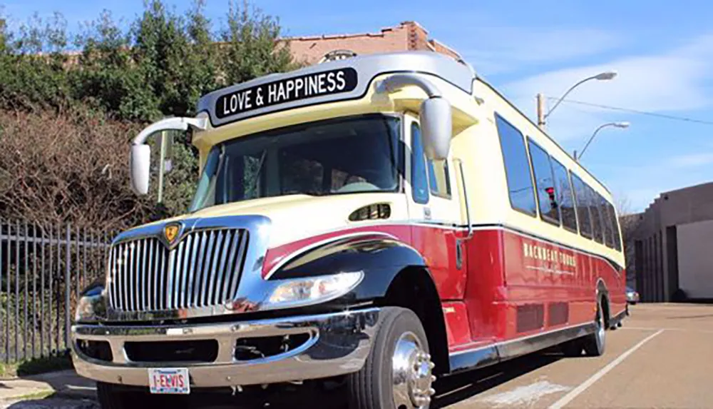 A colorful bus with the words LOVE  HAPPINESS on the signboard is parked at the side of a road with a personalized license plate that reads 1-ELVIS